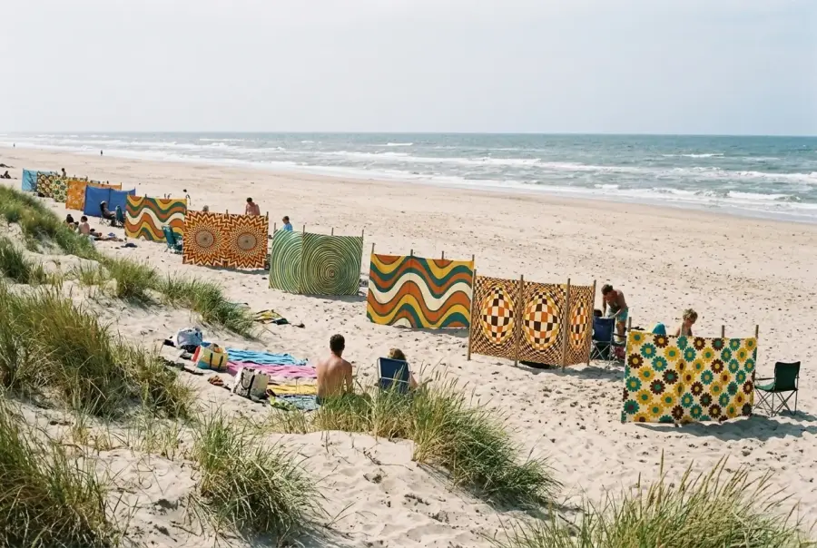 A row of VEYLISSEE windbreaks in different prints along a beach